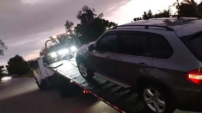 SUV being towed onto a flatbed tow truck on a dark road.