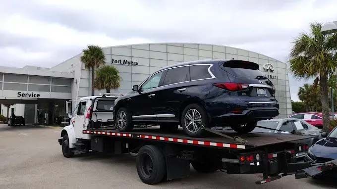Dark SUV on a tow truck in front of Fort Myers Infiniti dealership.