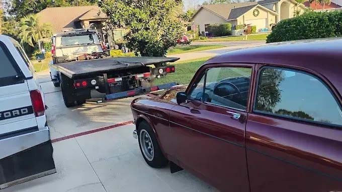 Red classic car being loaded onto a flatbed tow truck in a driveway.
