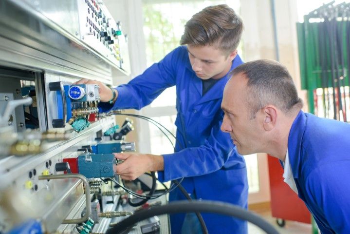 Two men in blue coveralls examining machinery in a workshop.