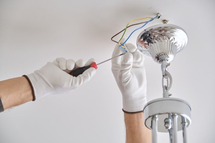 Person in gloves wiring a chrome chandelier to ceiling electrical wires.