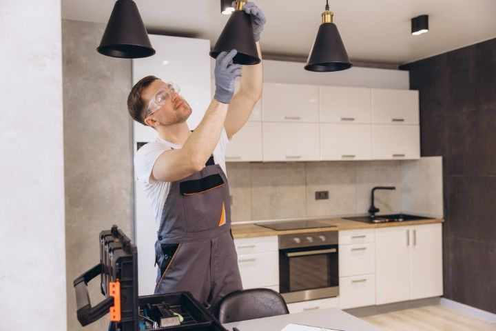 Man in overalls and safety glasses installing a pendant light in a kitchen.