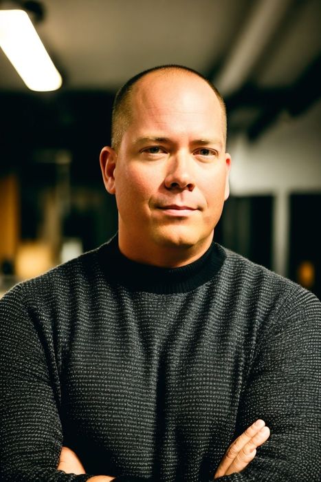 A  man in a black sweater is standing with his arms crossed.