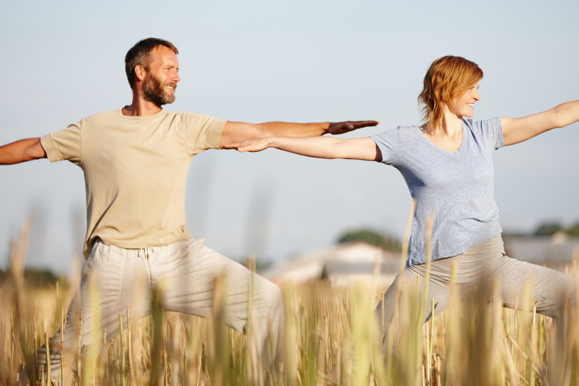 A man and a woman are practicing yoga in a field.