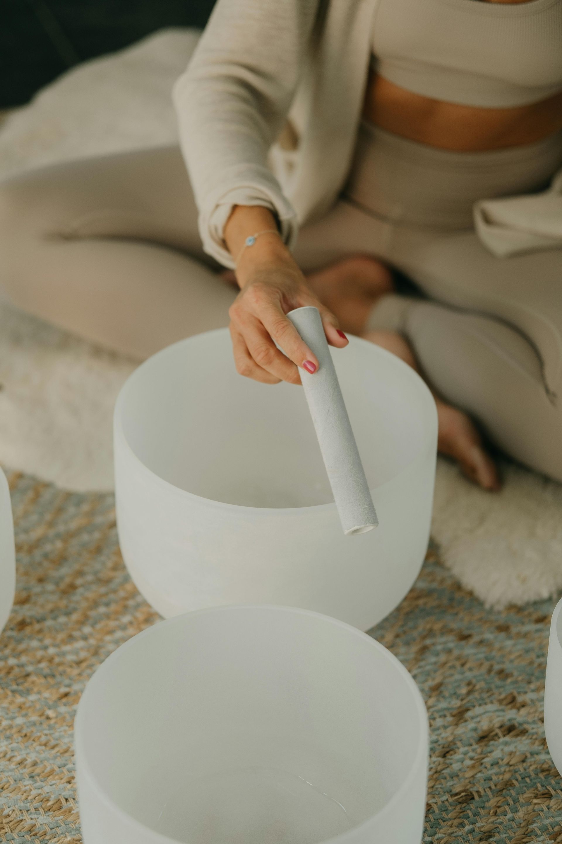 A woman is sitting on the floor playing a sound bowl.