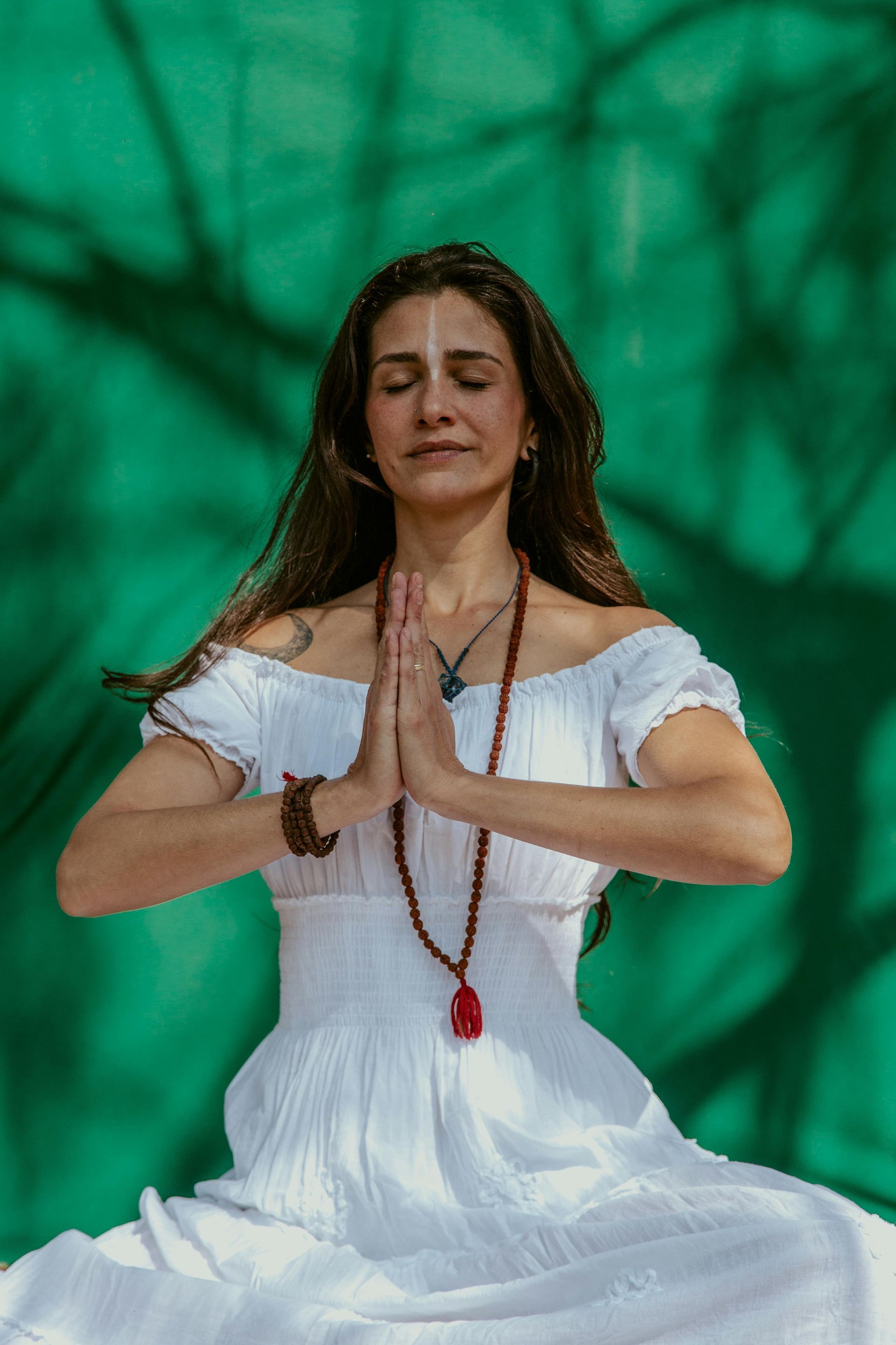 A woman in a white dress is sitting in a lotus position with her eyes closed.
