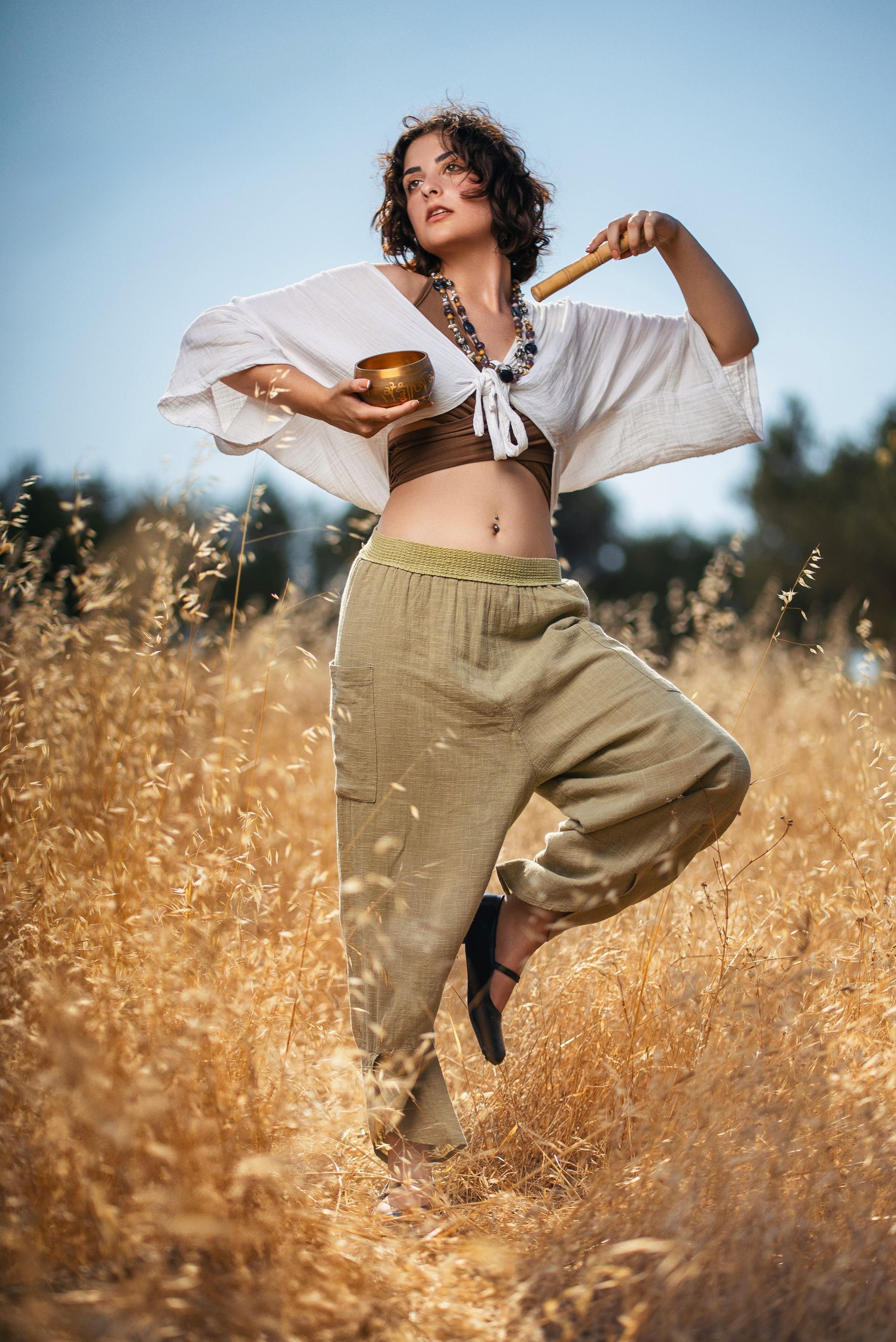 A woman is standing in a field holding a bowl and a wooden stick.