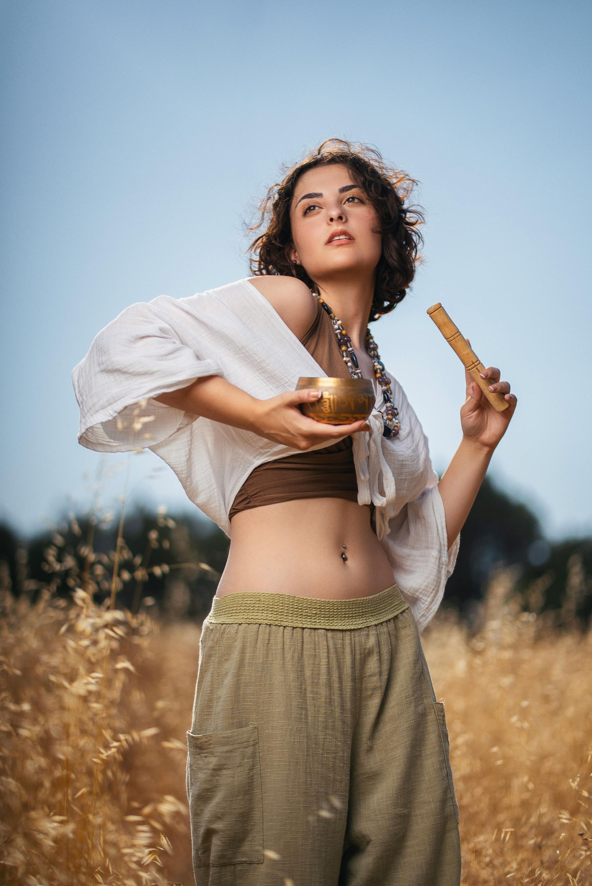 A woman is standing in a field holding a bowl and a stick.