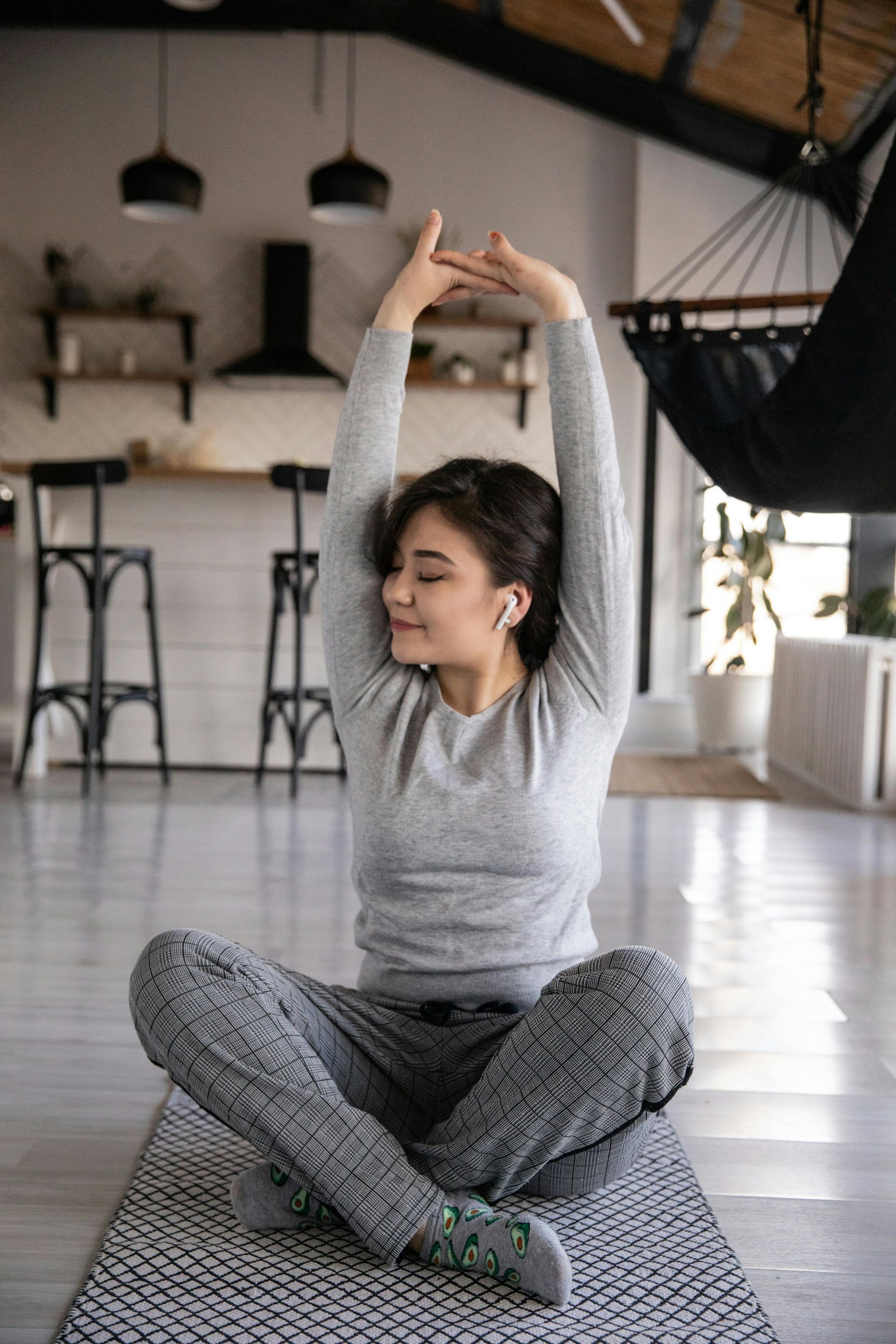 A woman is sitting on a yoga mat with her arms outstretched.