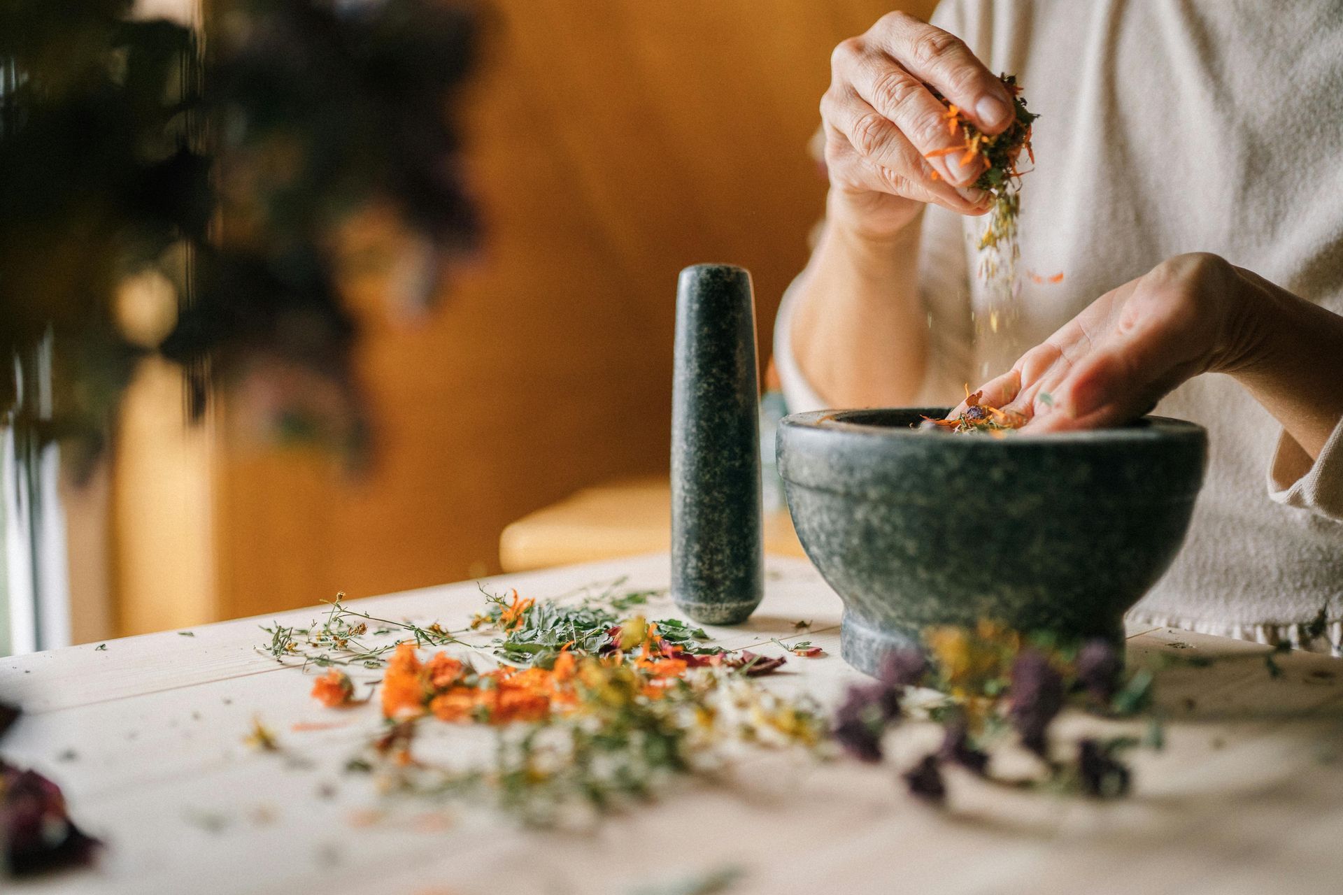 A person is using a mortar and pestle to mix herbs in a bowl.