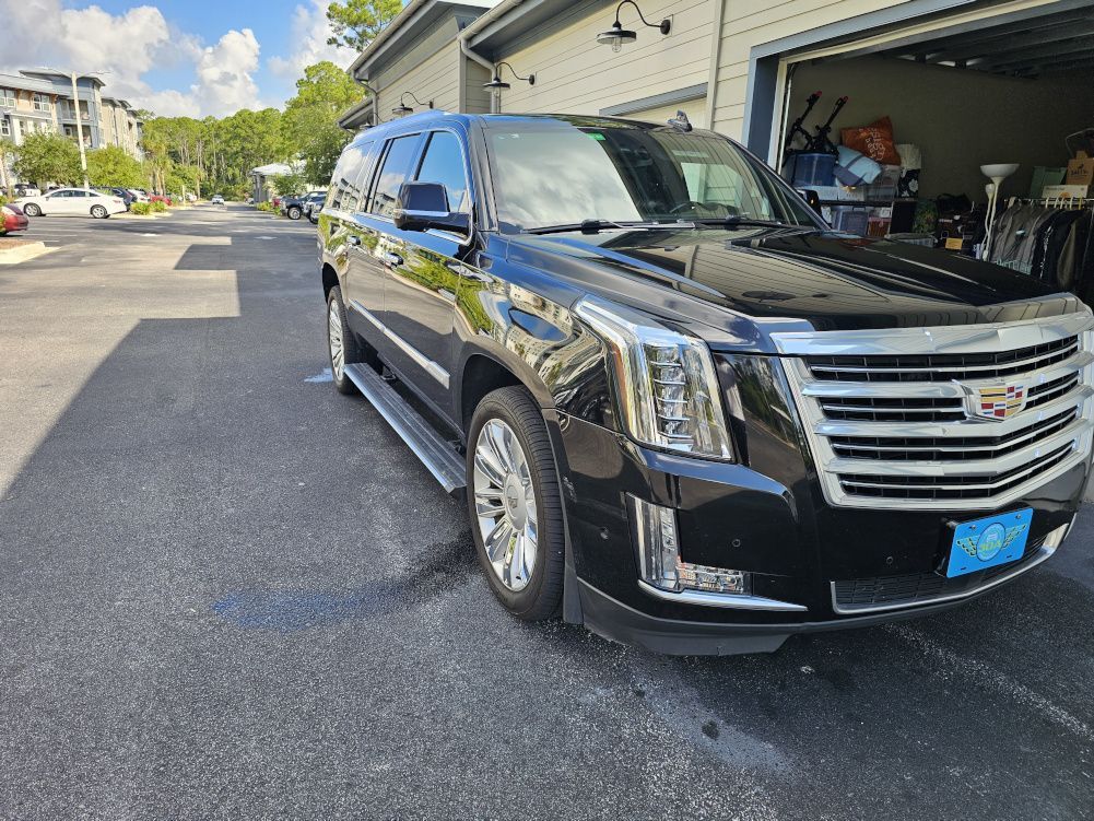Black Cadillac Escalade parked on asphalt driveway, in front of a garage and apartments.