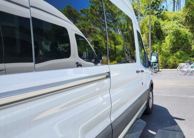 White van parked outside, reflecting trees, with open sliding door.