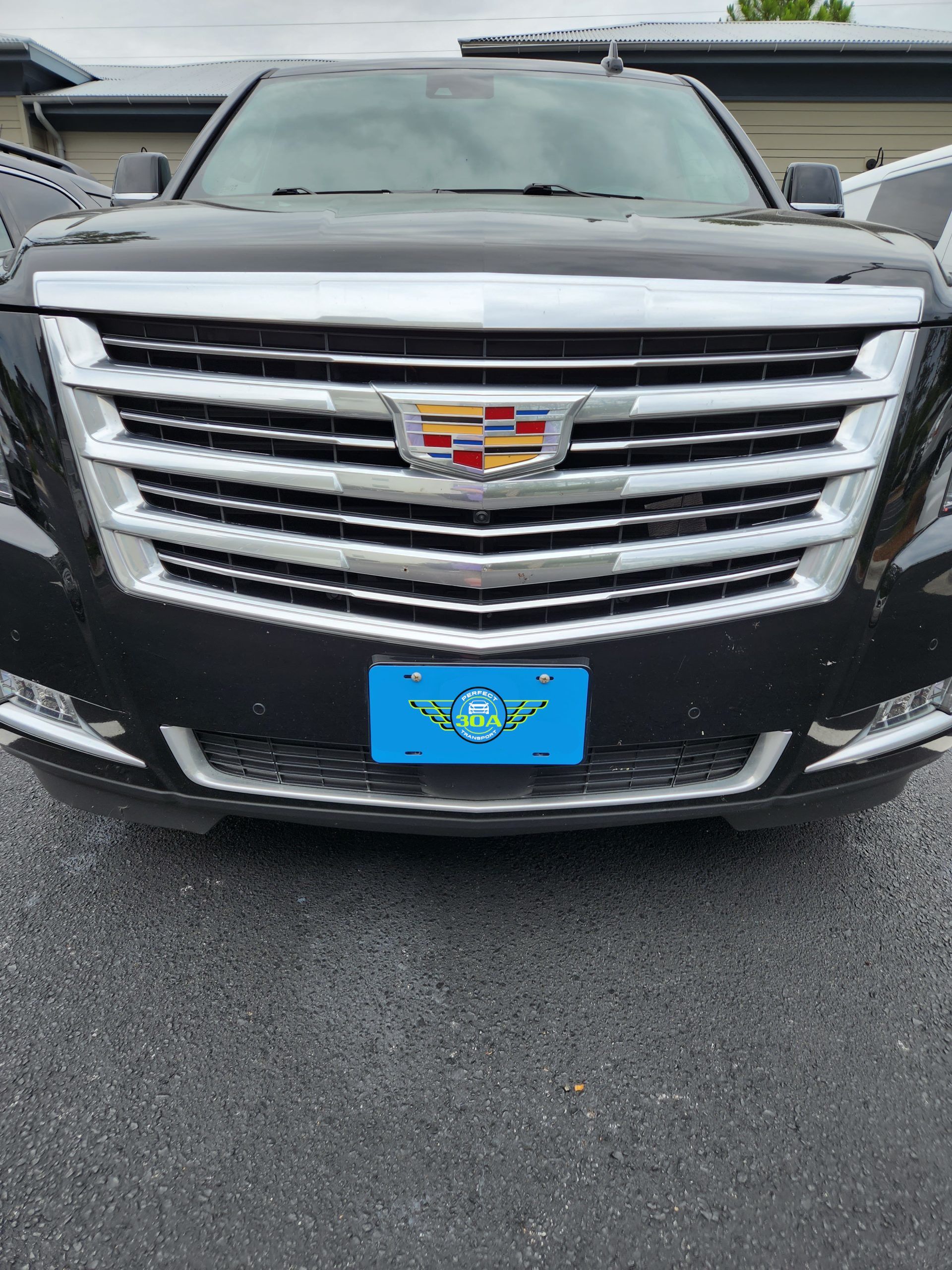 Cadillac SUV front view, showing grille with license plate; dark gray with a blue license plate.