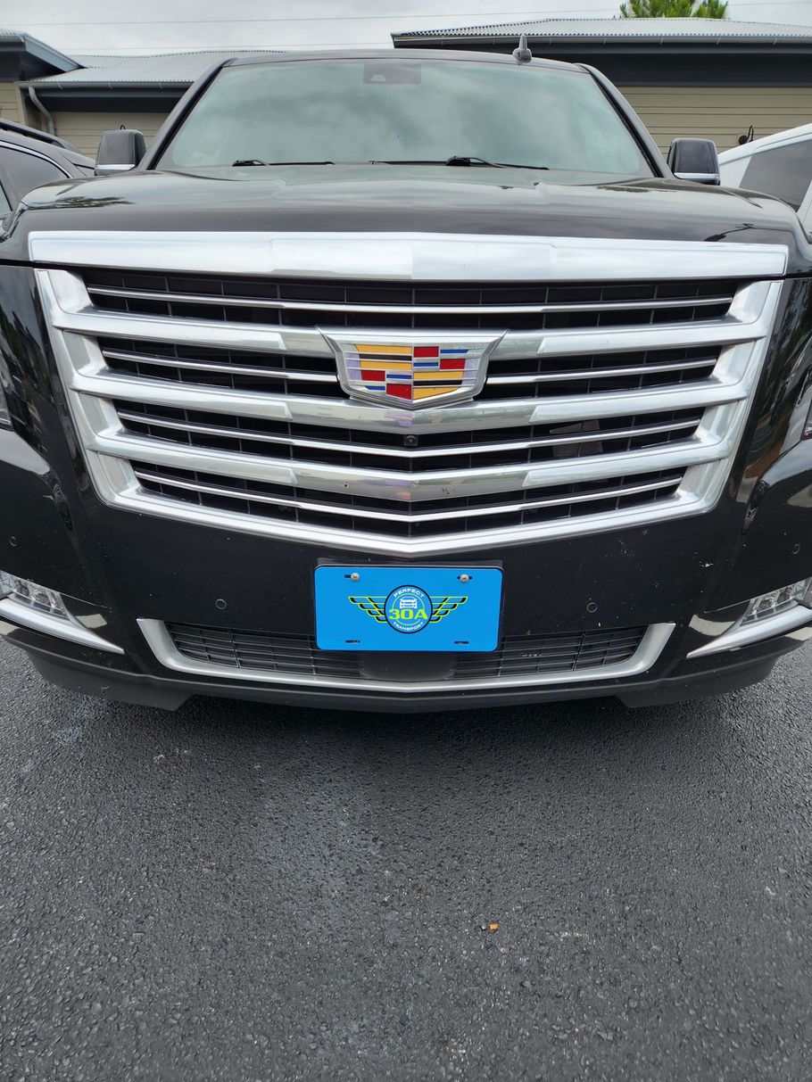 Black Cadillac SUV with a chrome grill and blue license plate parked outside.