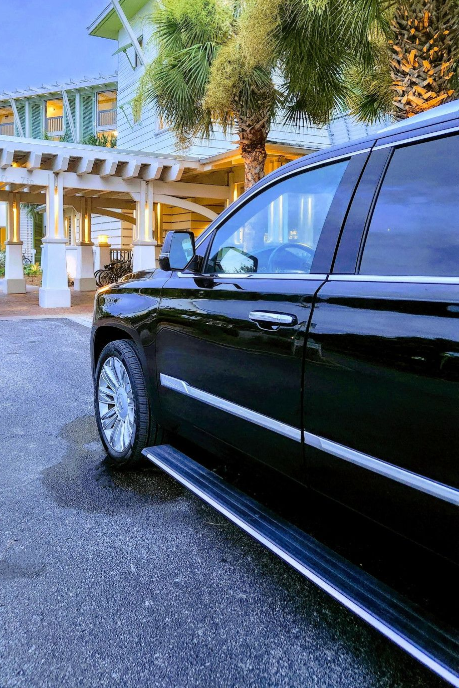 Black SUV parked at a light-colored building entrance with a pergola and palm trees.
