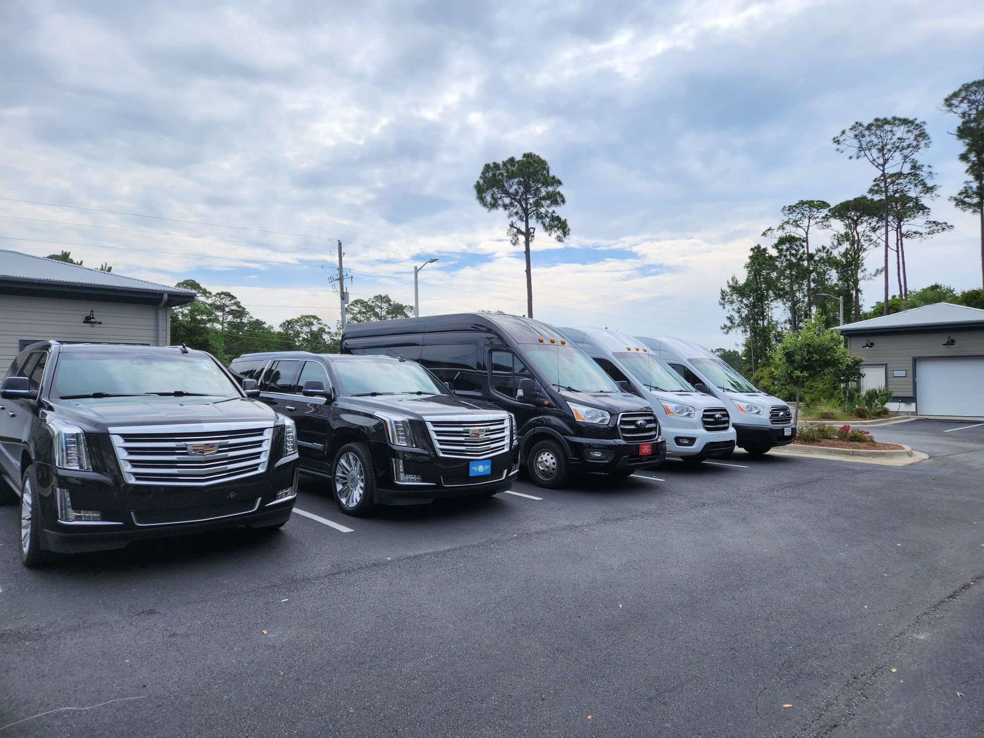 Several black vehicles parked outdoors on a gray day. Includes SUVs and vans.