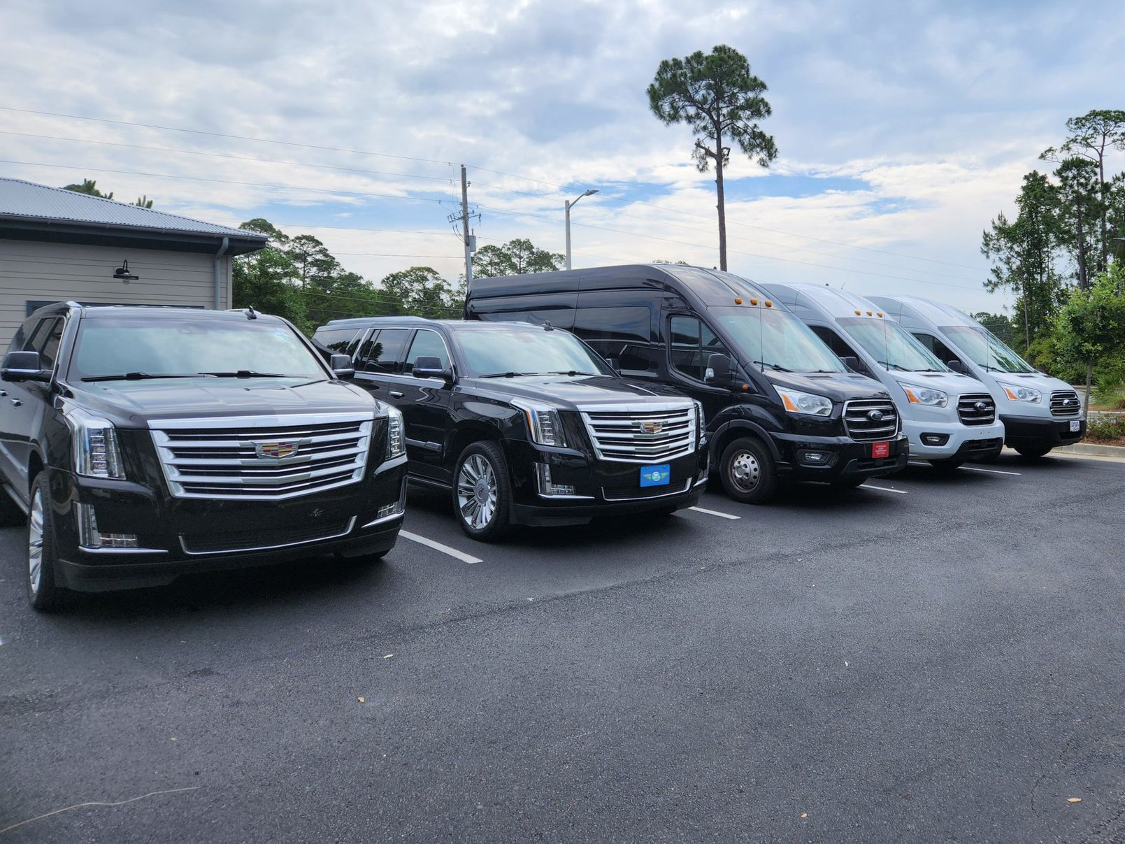 Two black Cadillac Escalades parked in an asphalt parking lot, in front of a multi-story building.