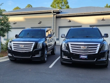 Two black Cadillac Escalades parked in front of a building with garage doors.