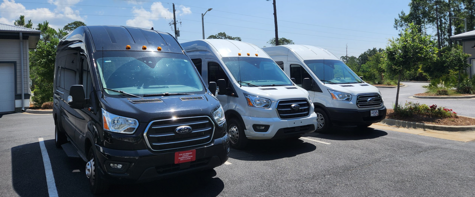 White Ford Transit van parked outside a store on a sunny day. A black pickup truck is in the background.