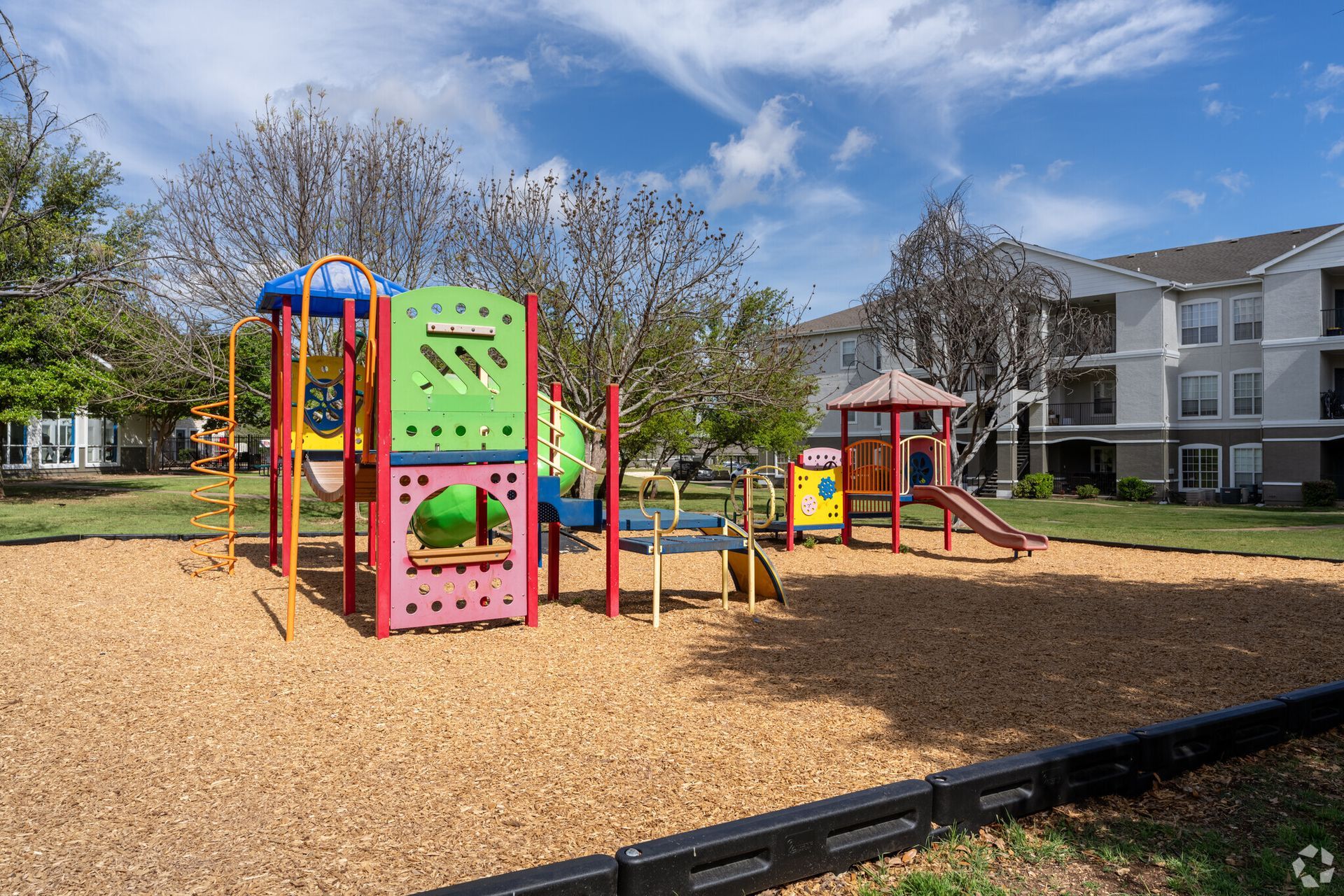 A colorful playground in a park with a building in the background.