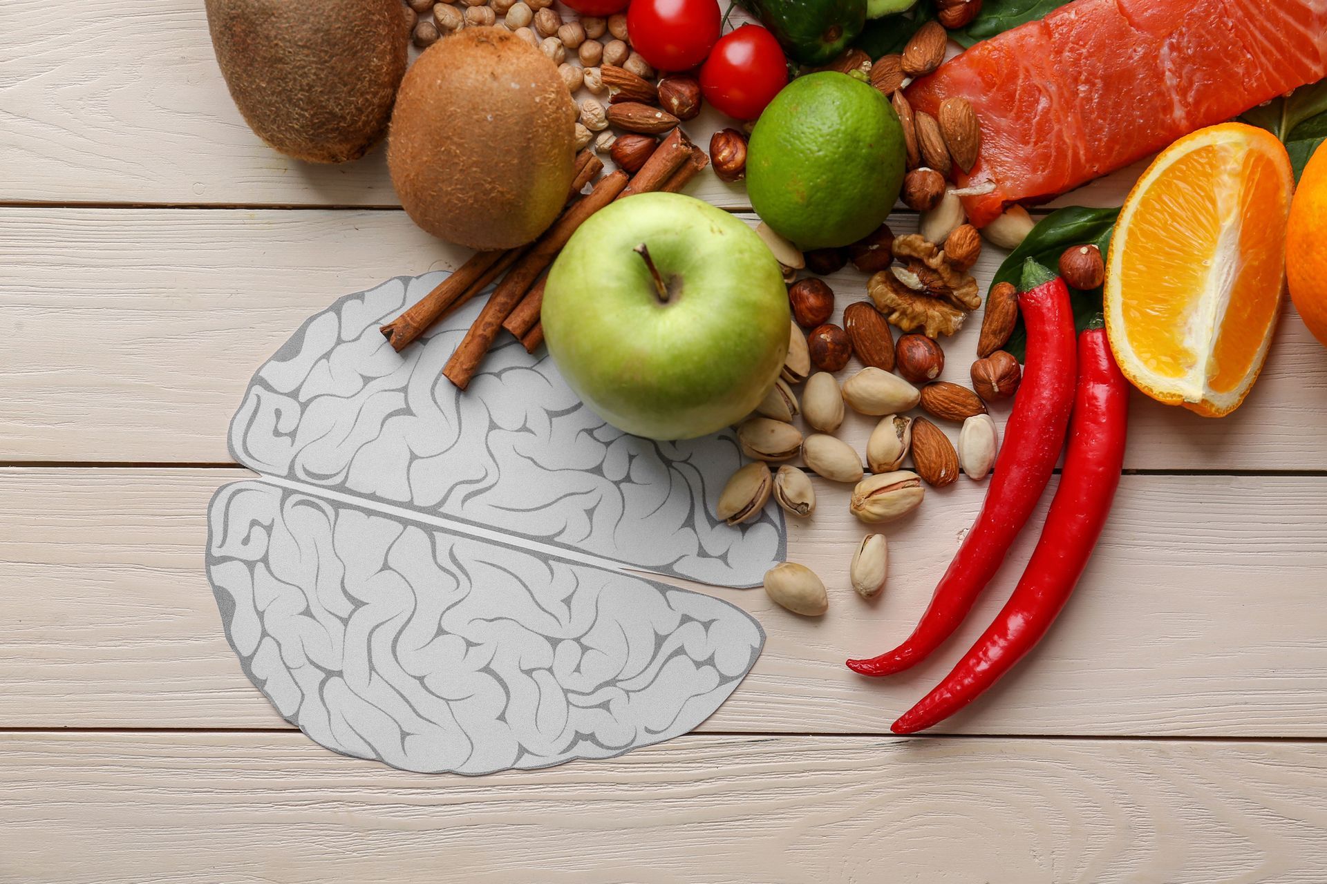 Sagoma del cervello con frutta fresca, noci e salmone su una superficie di legno, a simboleggiare gli alimenti salutari per il cervello.