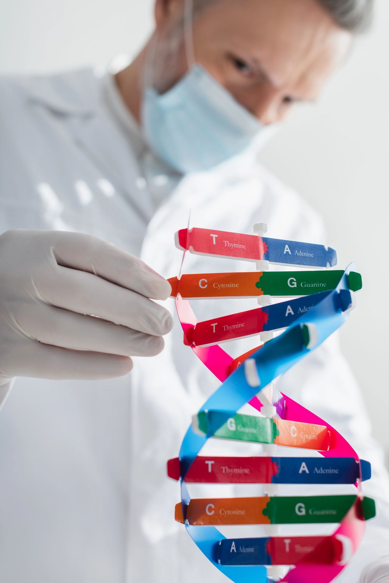 Scienziato in camice e mascherina che tiene in mano un modello di DNA colorato.