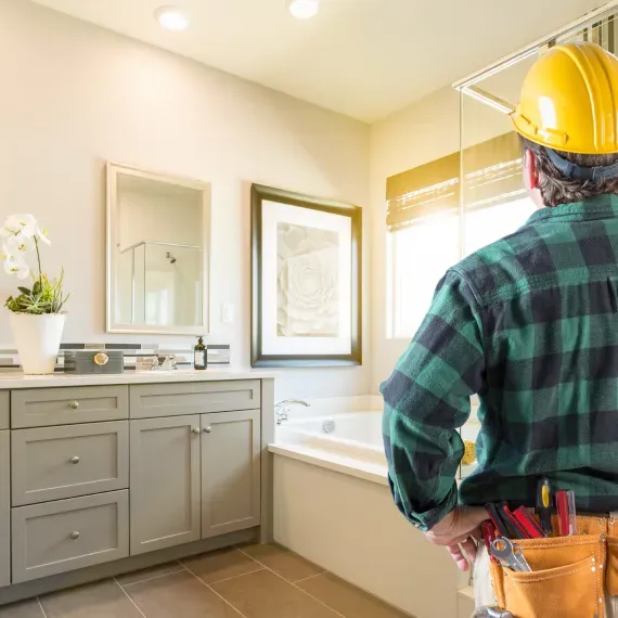 A man wearing a hard hat is standing in a bathroom.