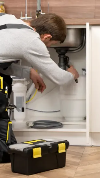 A plumber is fixing a sink in a kitchen.