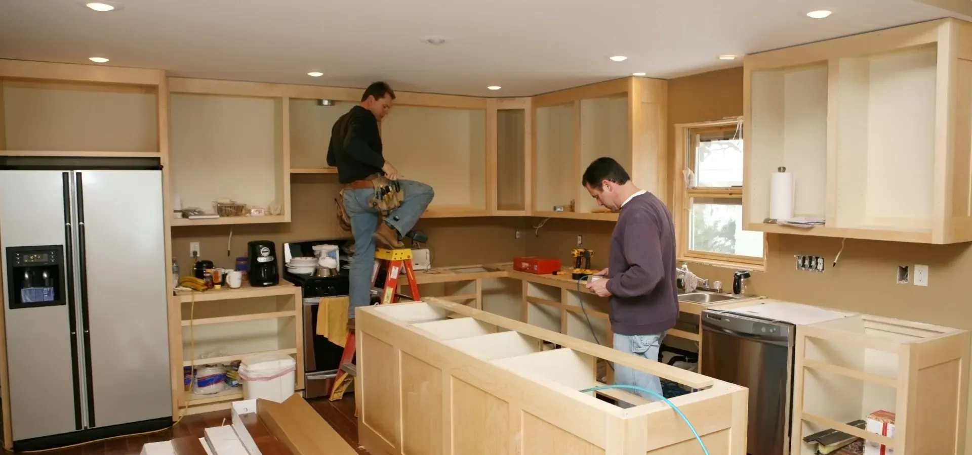 Two men are working on a kitchen in a house