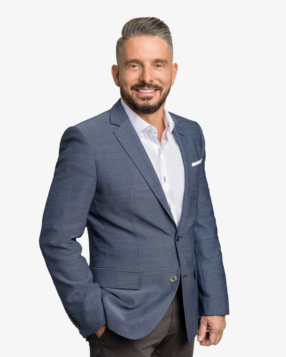 A professional headshot of a man with a short beard, smiling, wearing a blue patterned blazer over a white shirt.