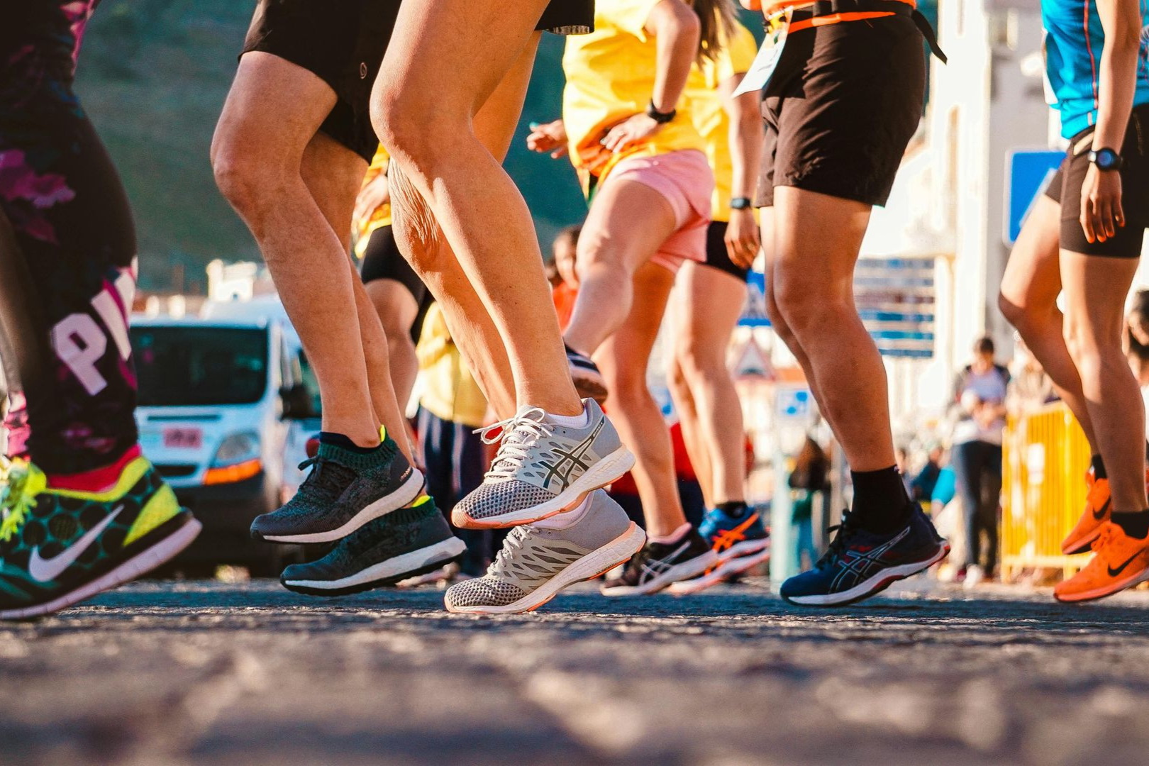 Group of runners wearing athletic shoes and gear, captured mid-stride while racing on a paved road outdoors.