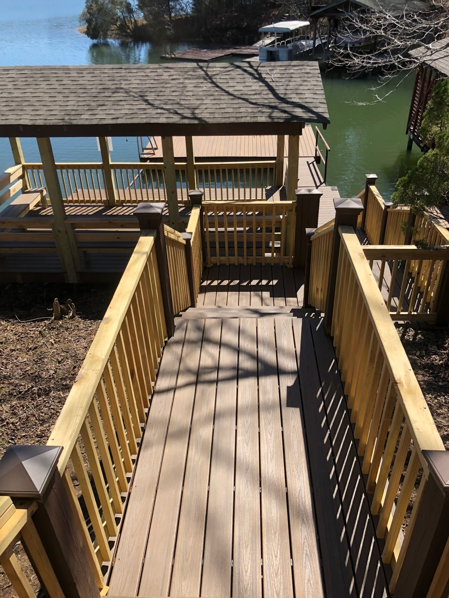 A new wooden deck with stairs and railings attached to the back of a light-colored brick house.