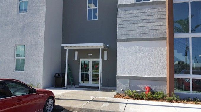 Exterior of a modern building with a red car parked in front. Entrance has a small awning.