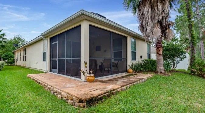 Screened patio attached to a beige house, surrounded by green grass and a palm tree.