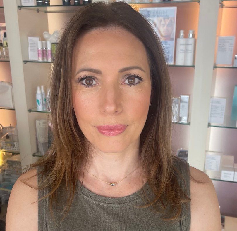 Woman with brown hair, wearing a green top, in front of a retail shelf of skincare products.