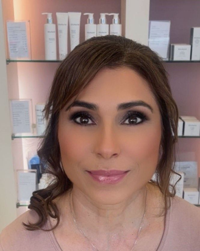 Woman with makeup in a skincare clinic, with a light pink top and products in the background.