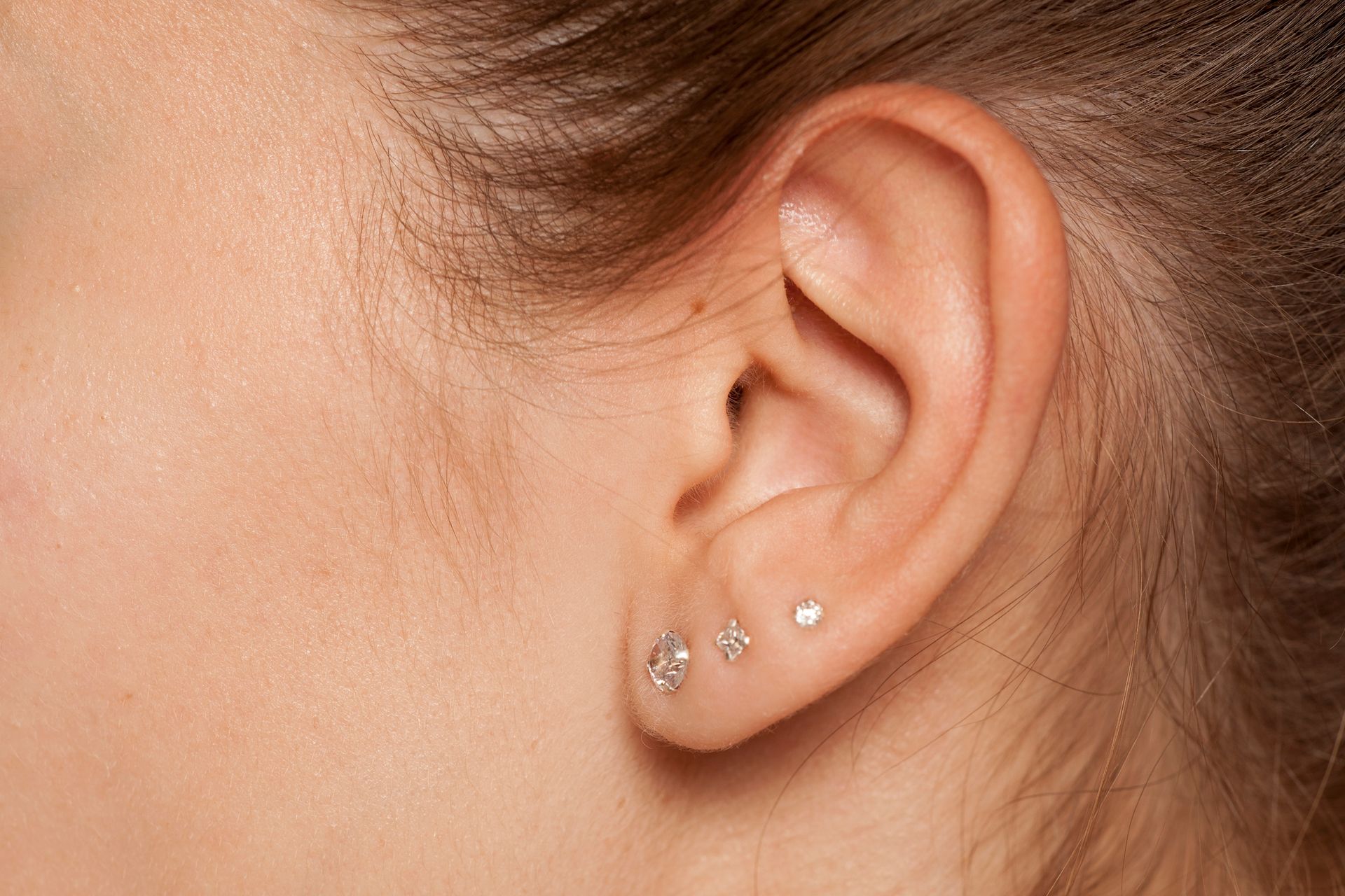 Close-up of a person's ear with three small, sparkling earrings.