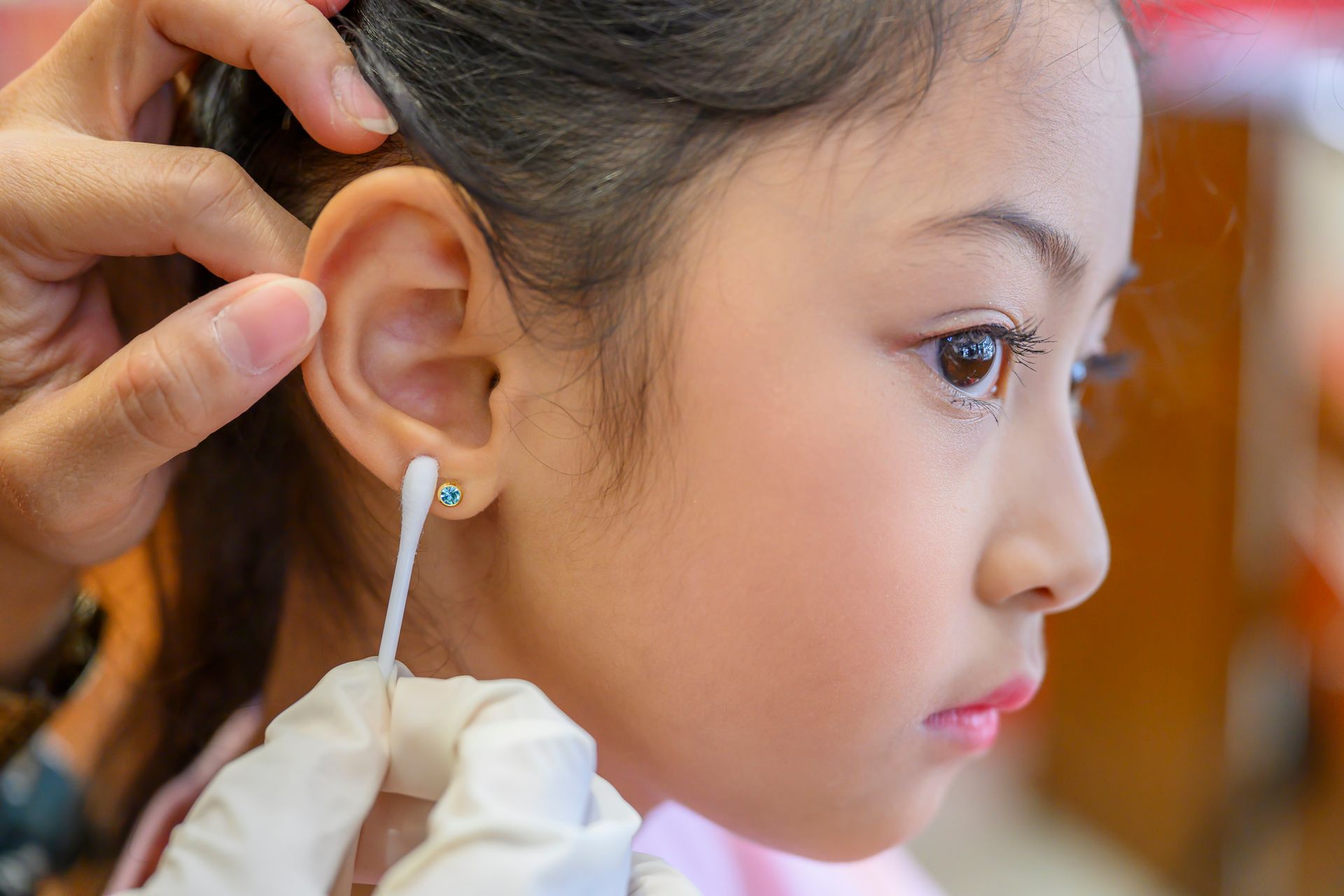 A girl's ear being cleaned with a cotton swab after an earring piercing. 