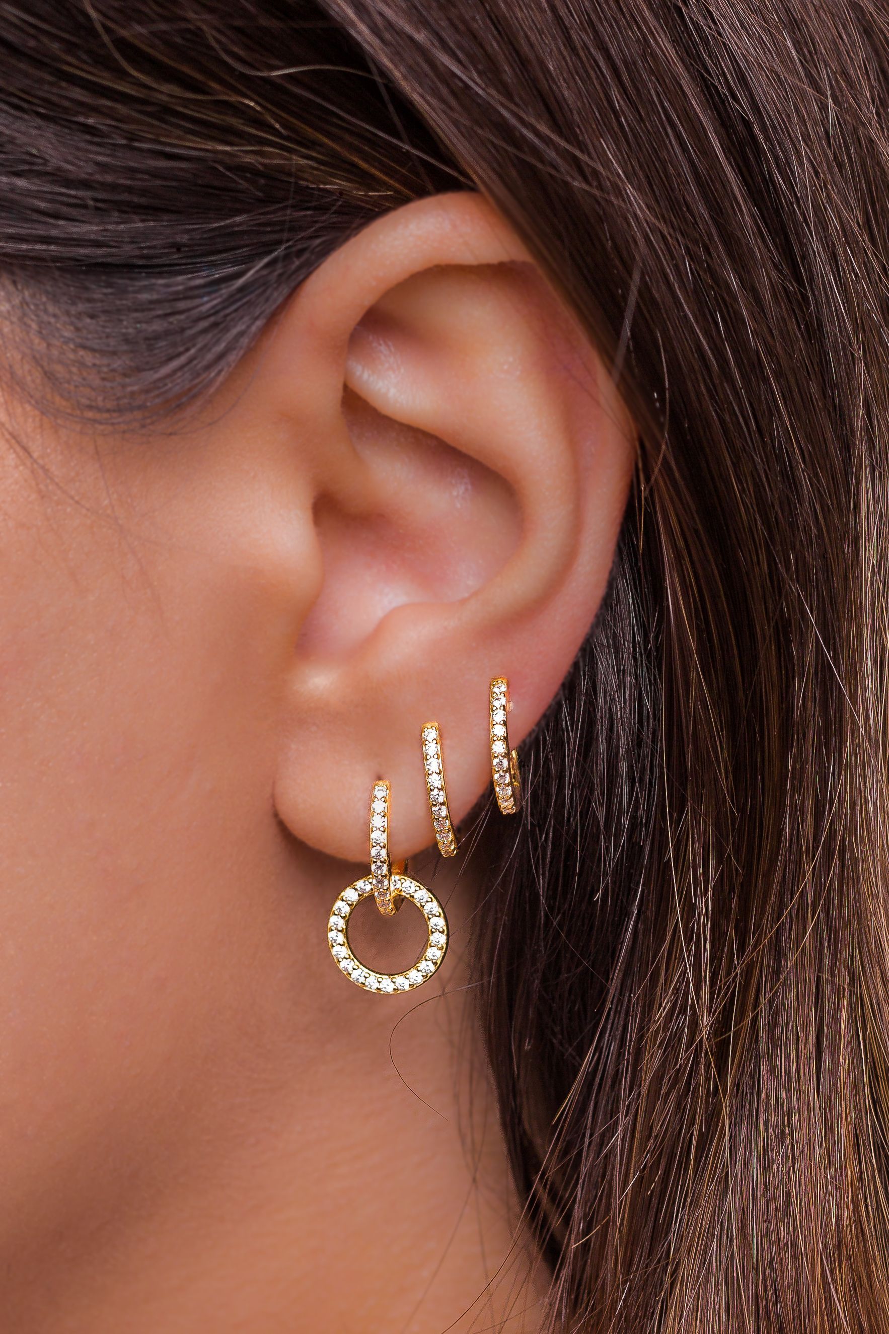 Woman's ear with three gold hoop earrings. 