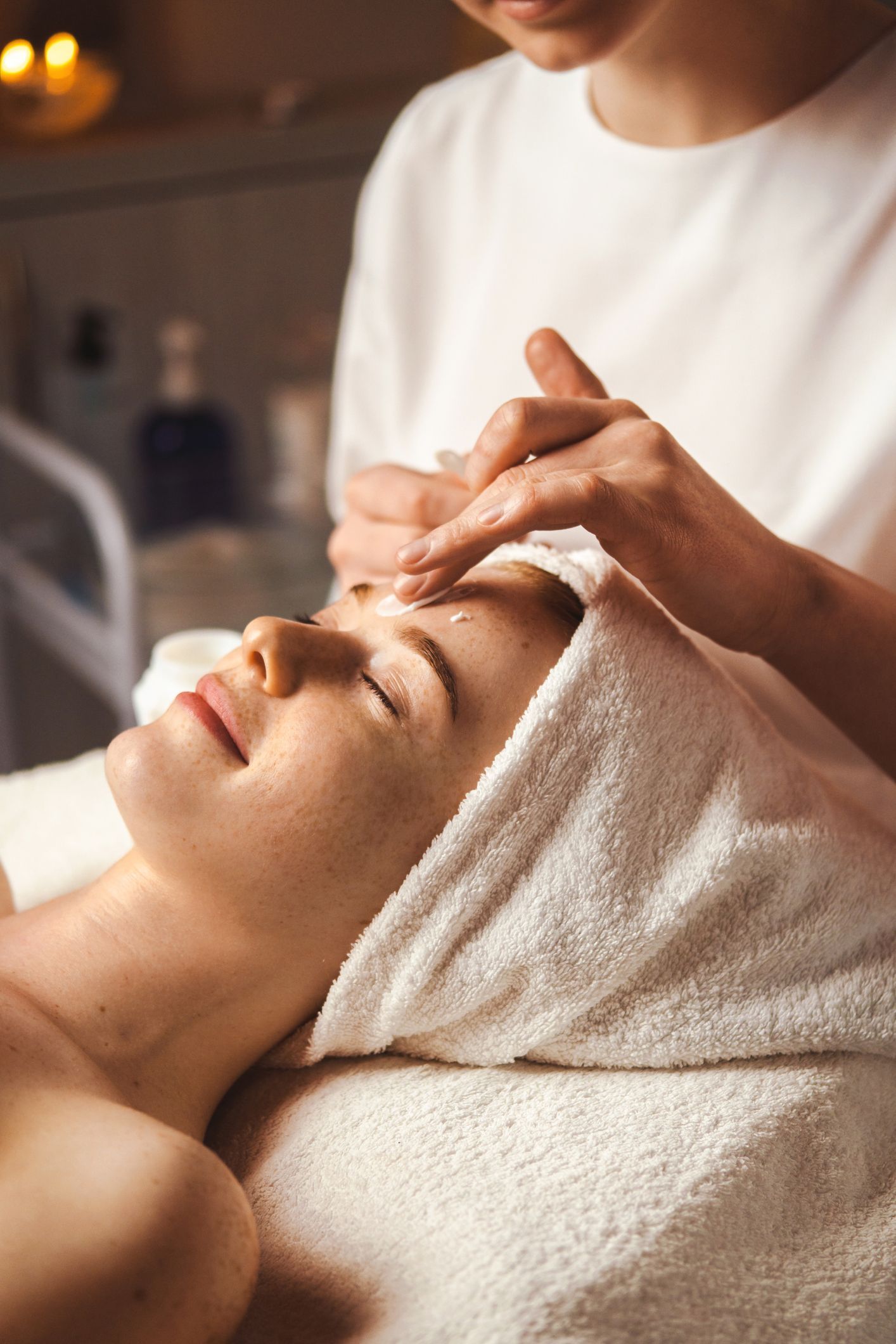 Woman receiving a facial, eyes closed, in a spa setting. 