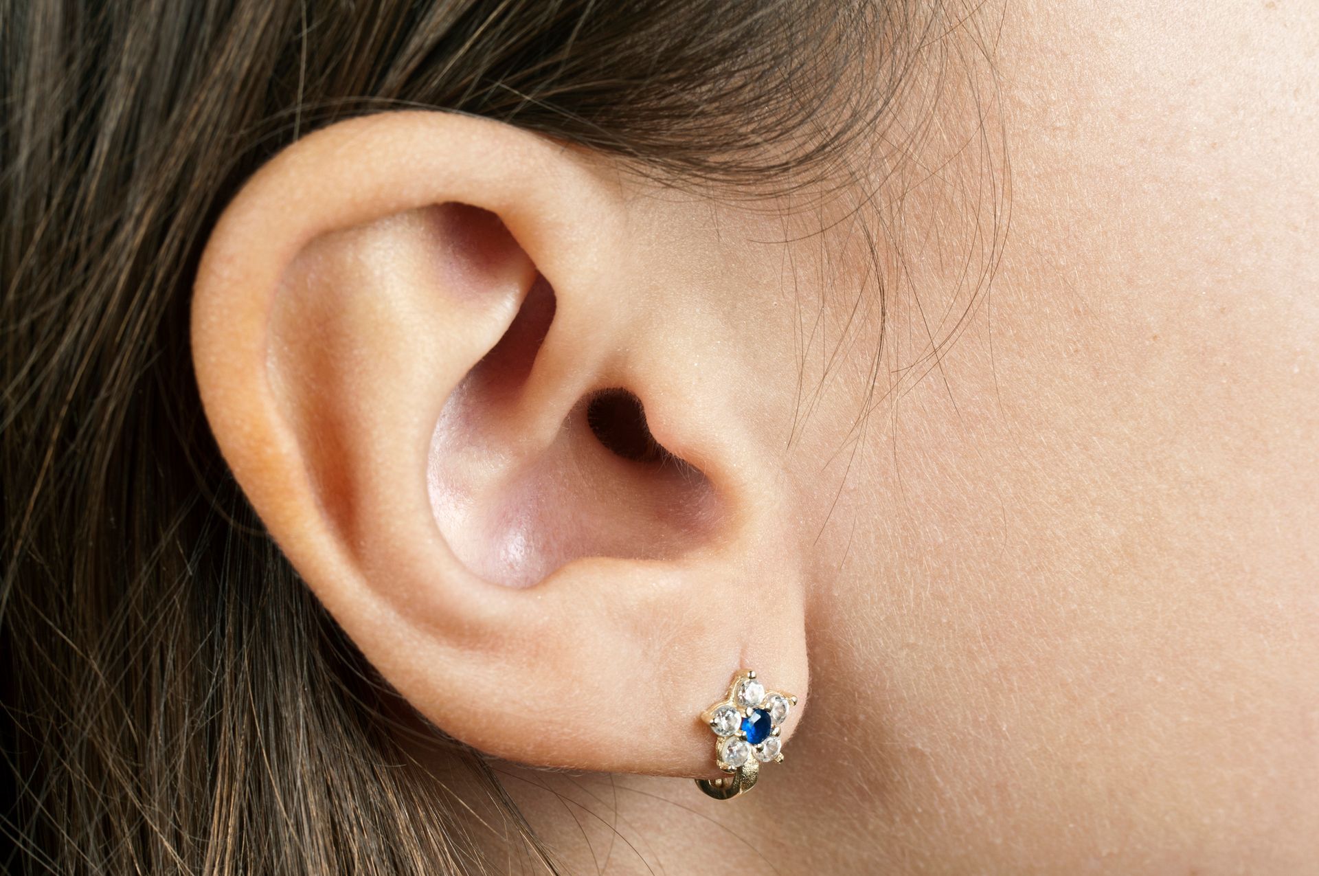 Close-up of a person's ear with a small gold earring with a blue center and white gems.