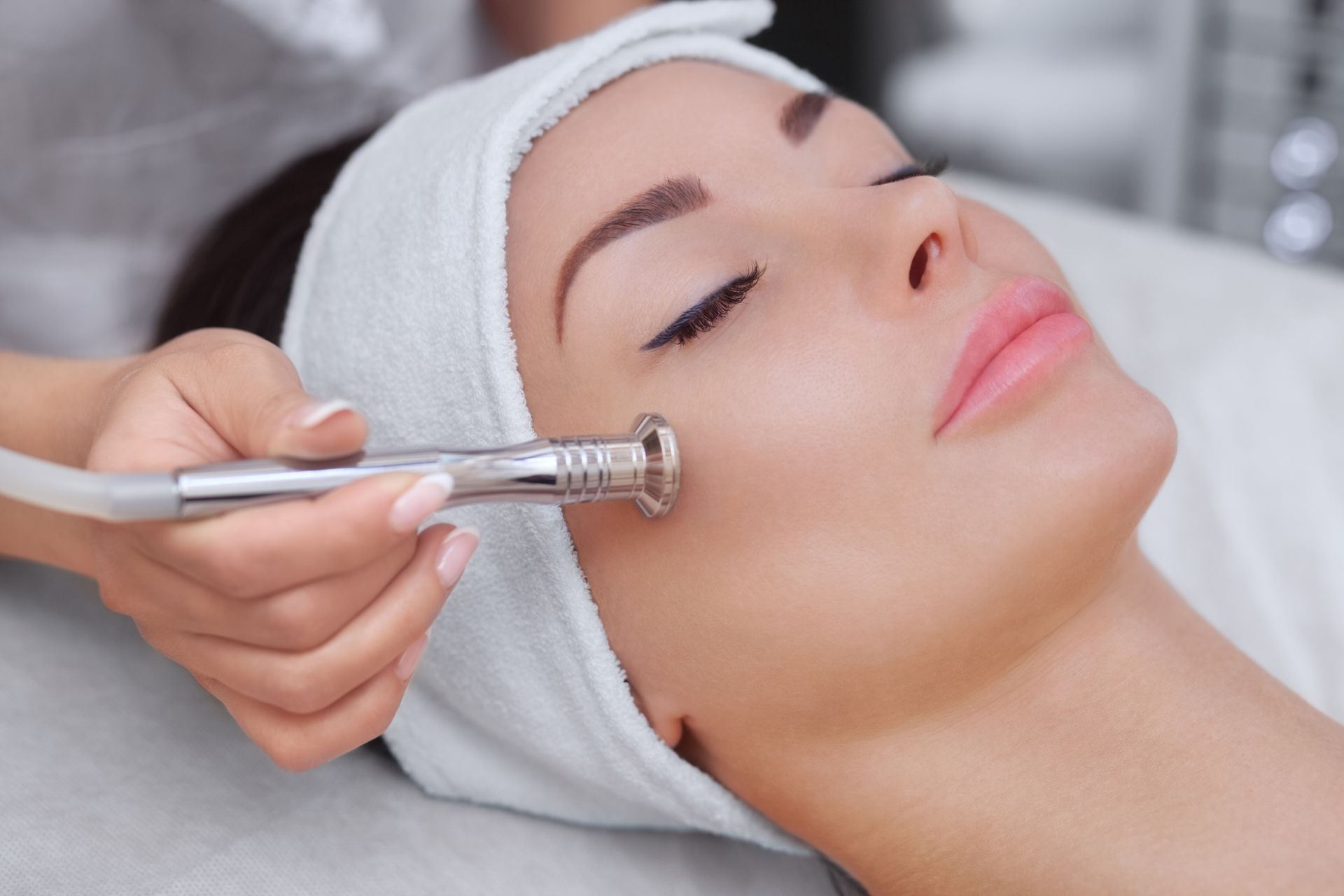 Woman receiving a facial treatment, using a handheld microdermabrasion.