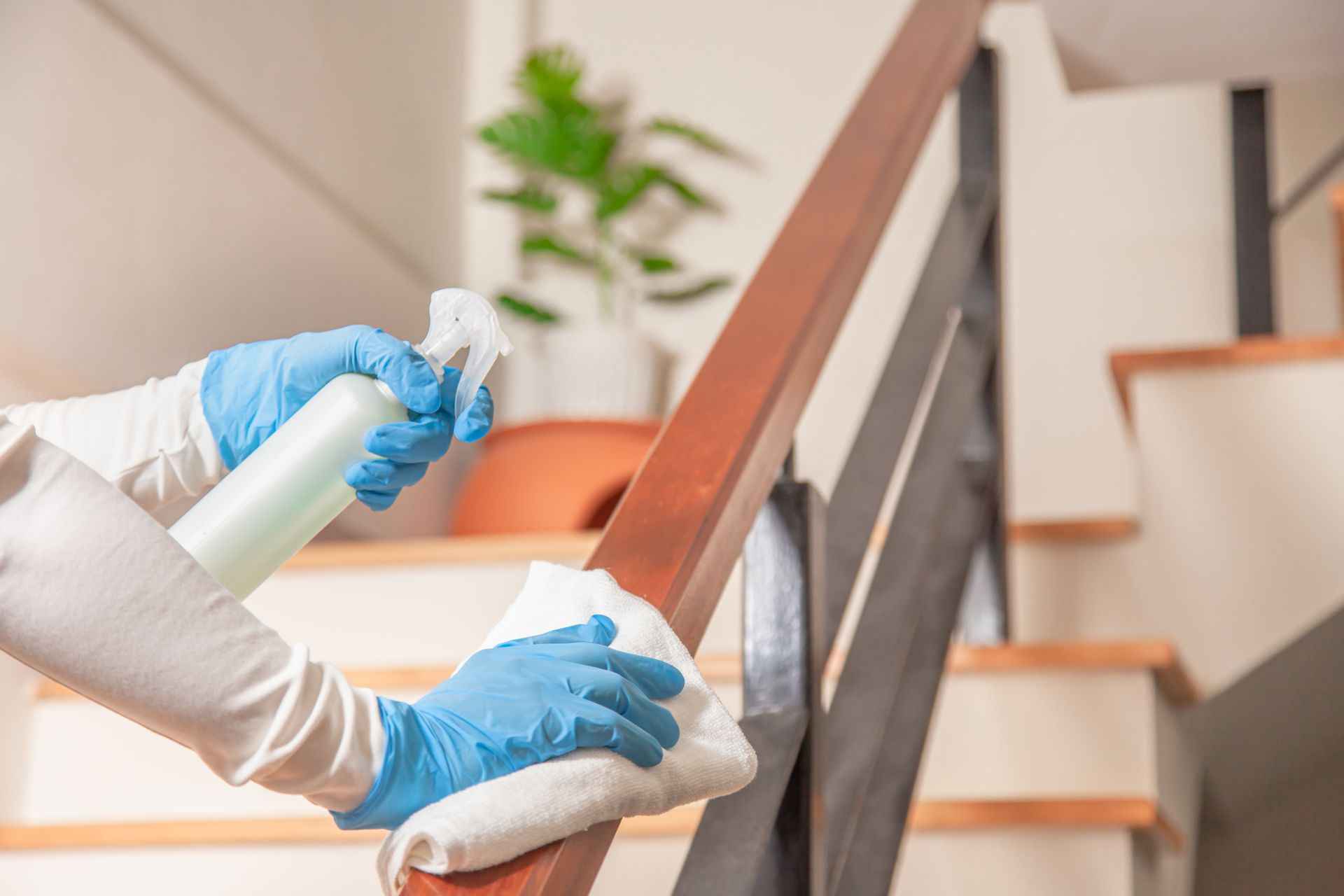 A person wearing blue gloves is cleaning the railing of a staircase.