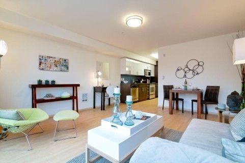 Bright and modern living room in H2O Apartments Seattle with large windows, light hardwood floors, gray sofa, and workspace desk