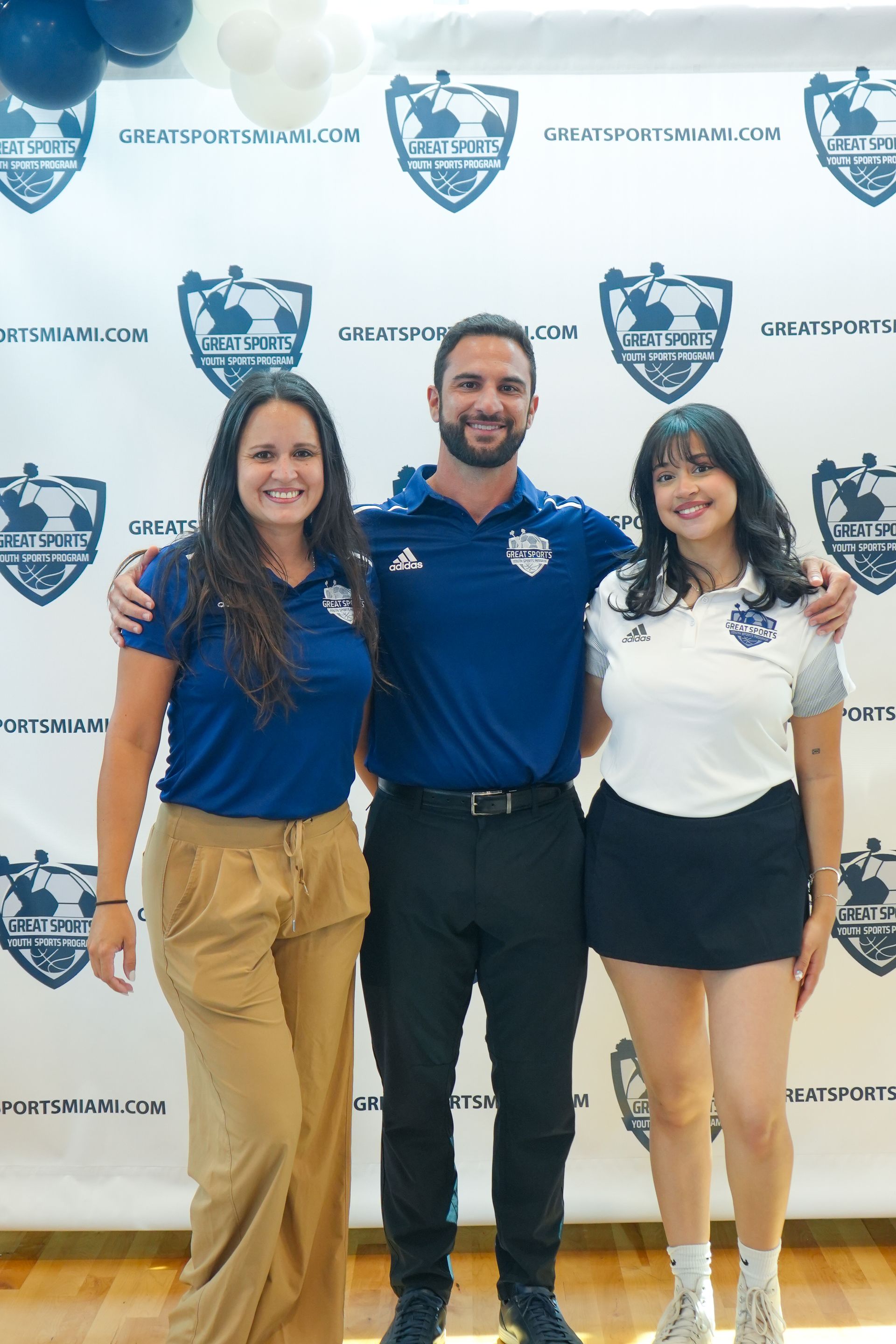 Three Great Sports team members smiling in front of a branded backdrop at an event or program launch