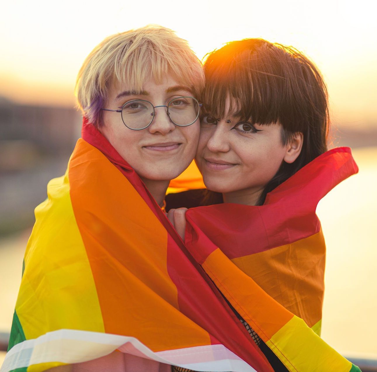 Two women are wrapped in a rainbow flag and hugging each other.