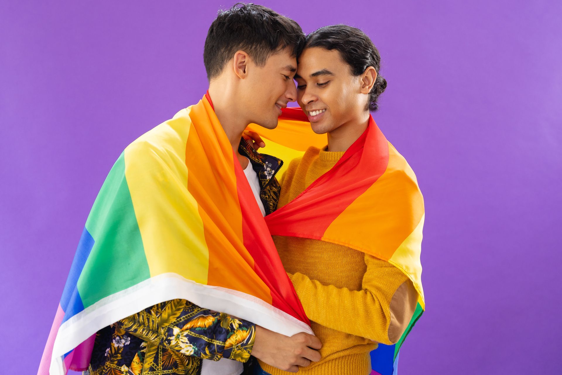two men are wrapped in a rainbow flag and hugging each other .