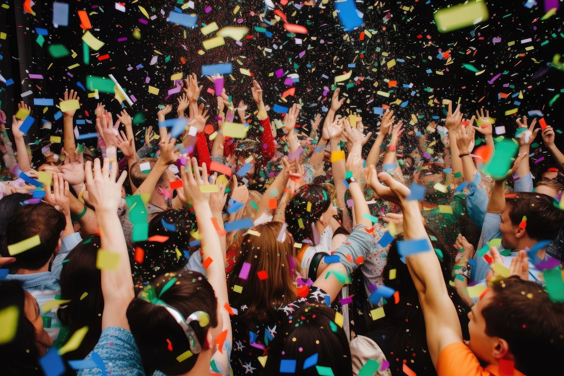 A crowd of people are raising their hands in the air while confetti is being thrown in the air.