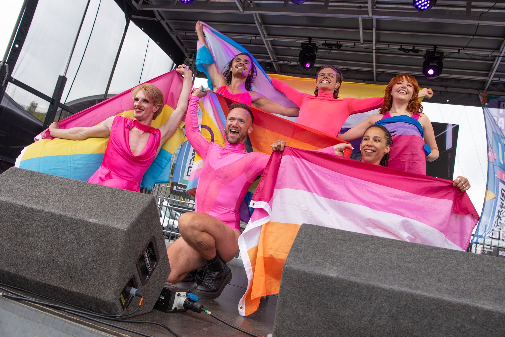 A group of people are holding rainbow flags on a stage.