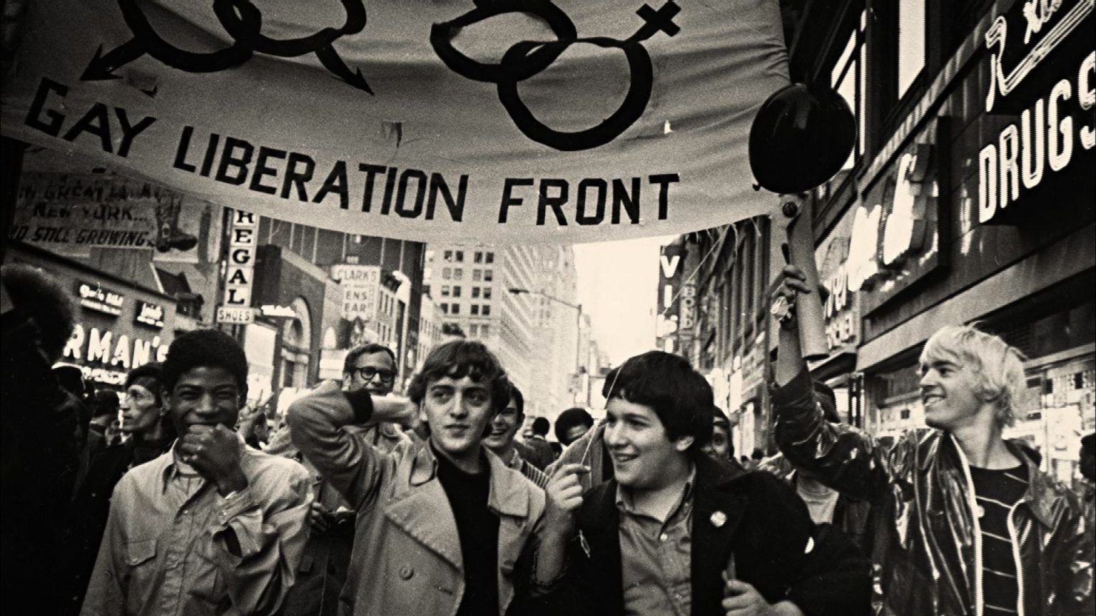 A group of people are walking down a street with a banner that says gay liberation front.